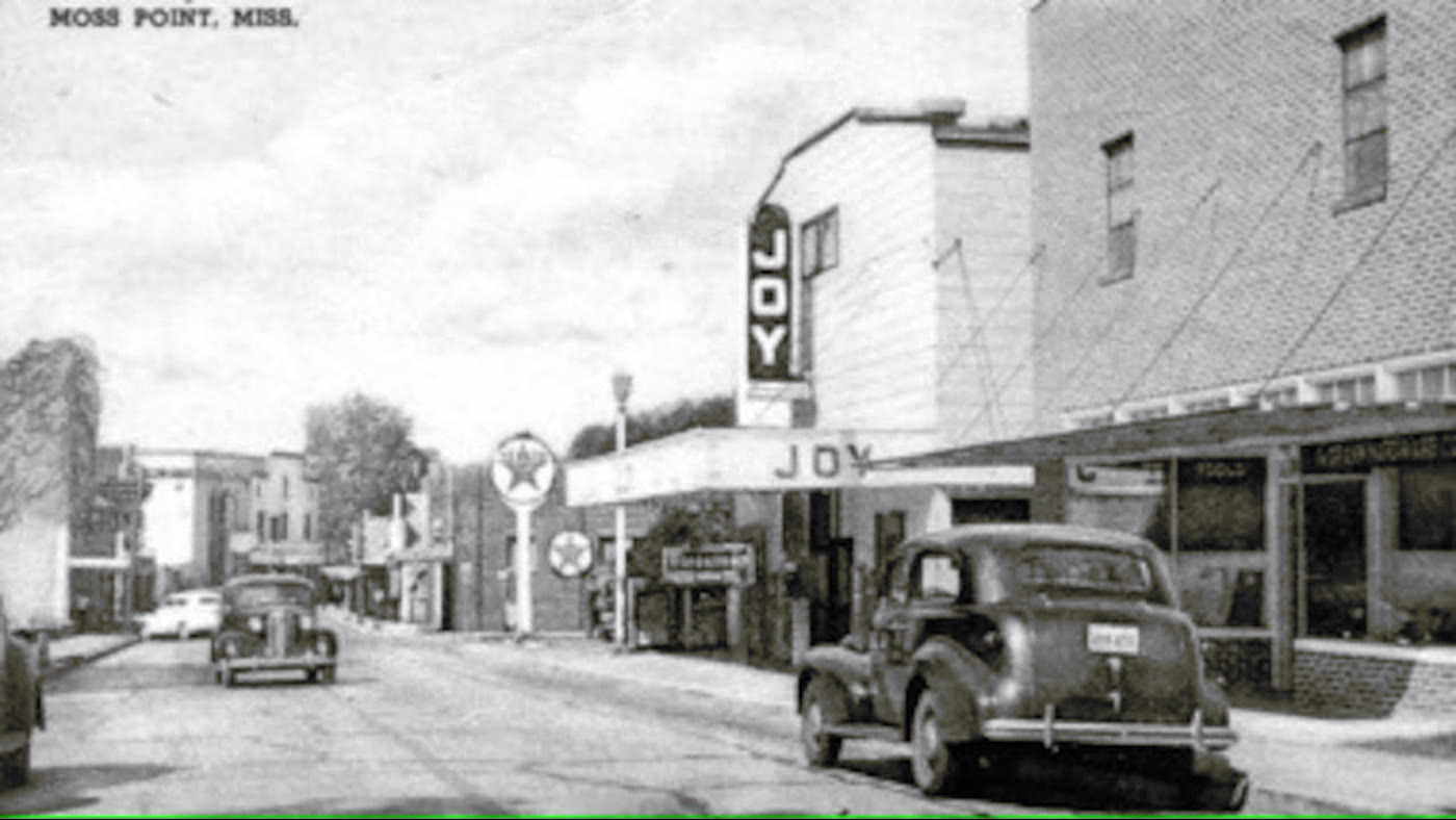 Downtown Moss Point's Main Street in the early-to-mid 1900s, with the Joy theater marquee, a Texaco station, and vintage cars